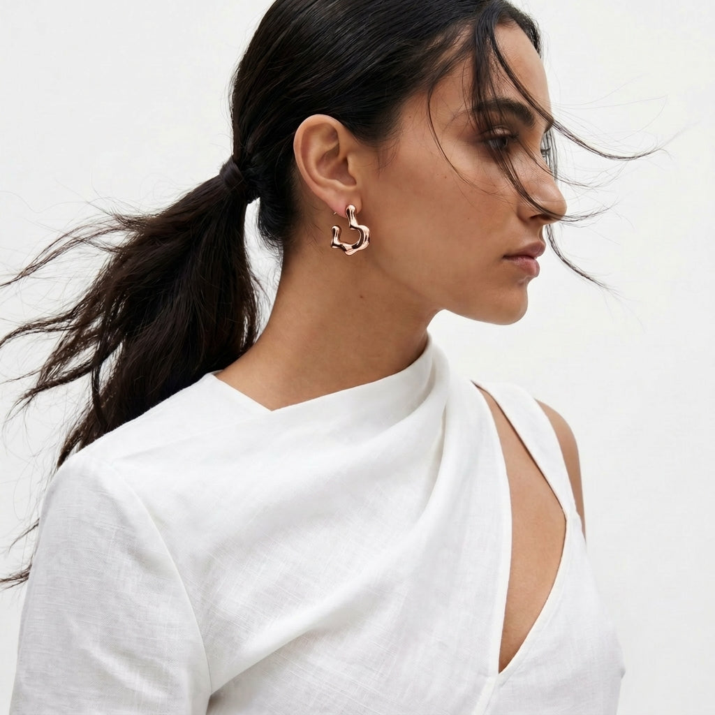 Woman wearing a white top with cut-out design on a plain background Rose gold hoop earrings on a light gray background premium stainless steel hypoallergenic, waterproof, tarnish-proof, and lightweight