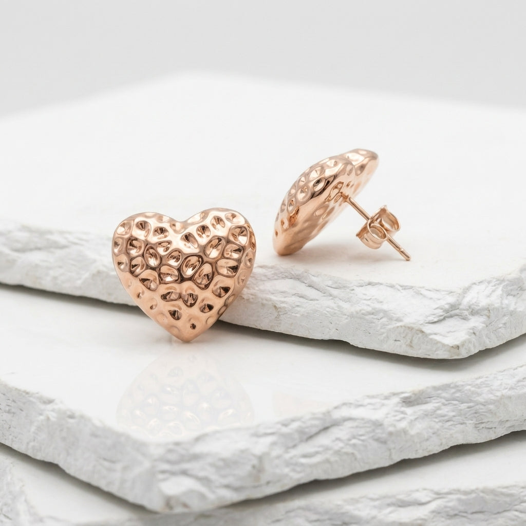 Rose gold heart-shaped earrings on a light stone surface Medium Rose Gold Amora Heart Stud Earrings premium stainless steel hypoallergenic, waterproof, tarnish-proof, and lightweight