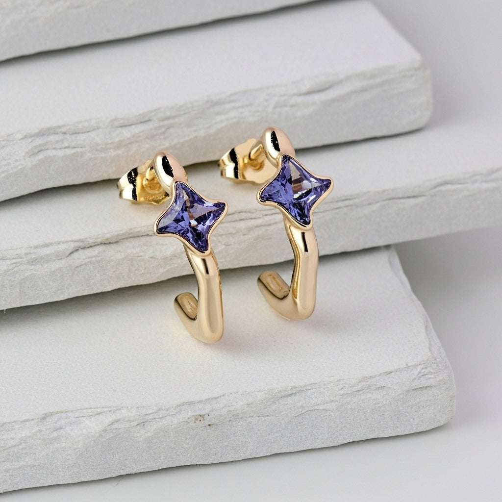 Gold earrings with purple gemstones on a light stone surface