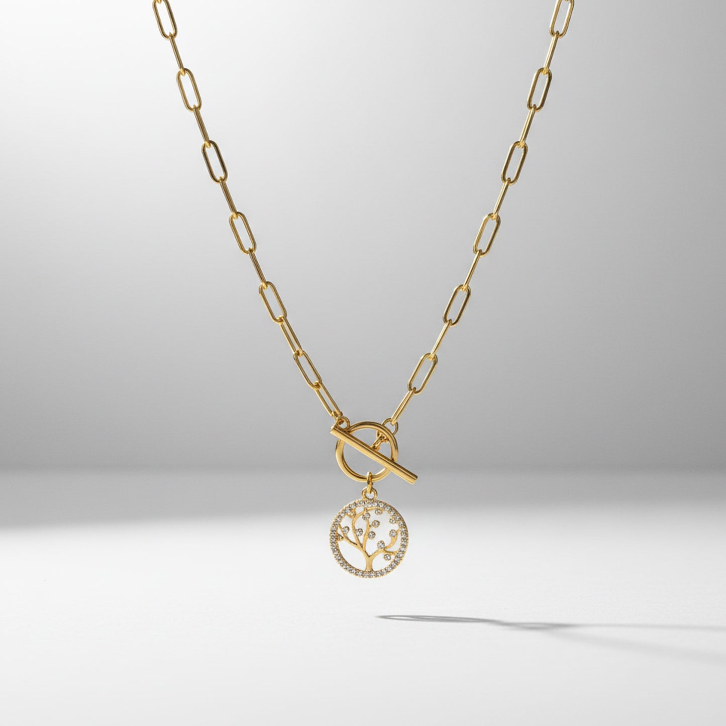 Gold necklace with a tree-of-life pendant on a light gray background
