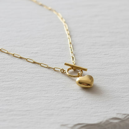 Gold paperclip necklace with a heart pendant on a light gray background