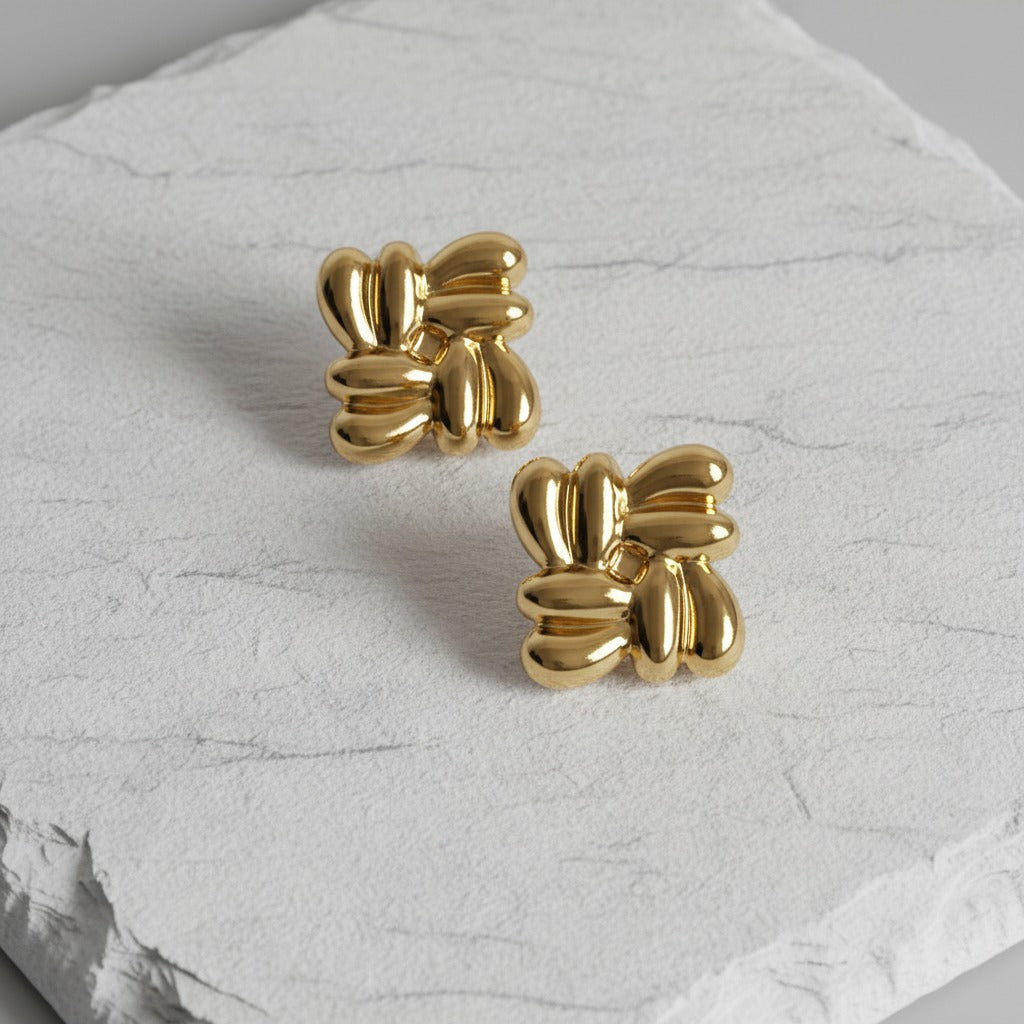 Gold bow-shaped earrings on a textured white surface