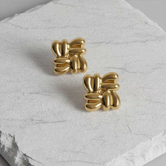 Gold bow-shaped earrings on a textured white surface