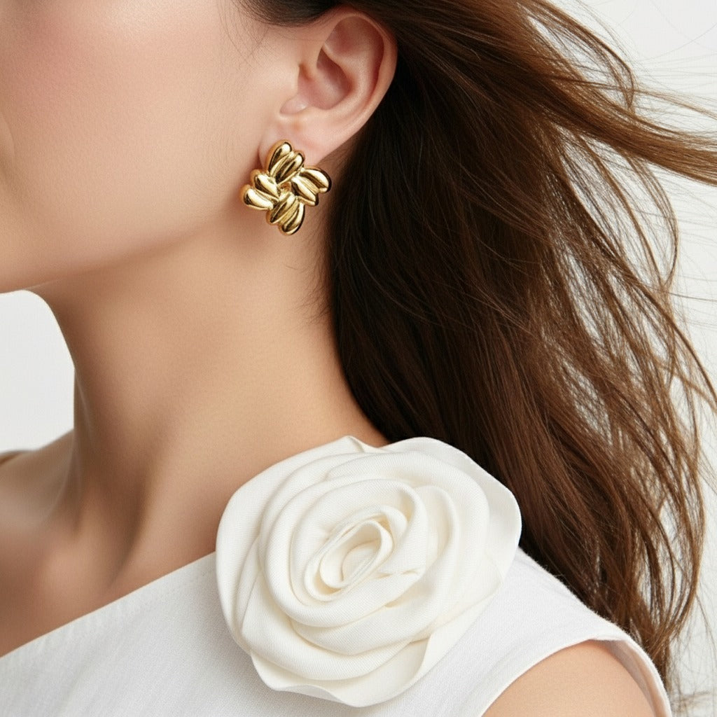 Gold earrings worn by a person with a white flower accessory.