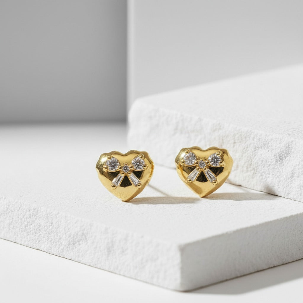 Gold heart-shaped earrings with bow design on a white surface