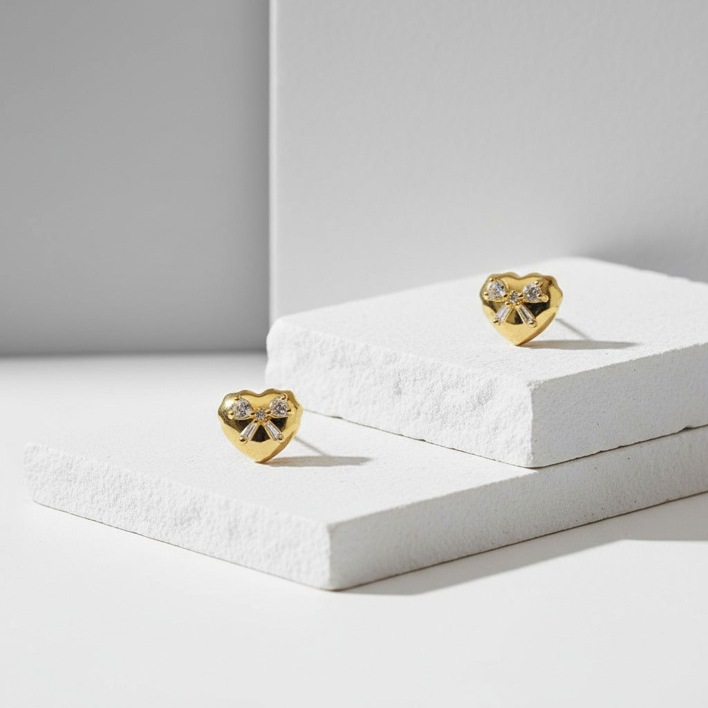 Gold heart-shaped earrings on a white surface with a gray background