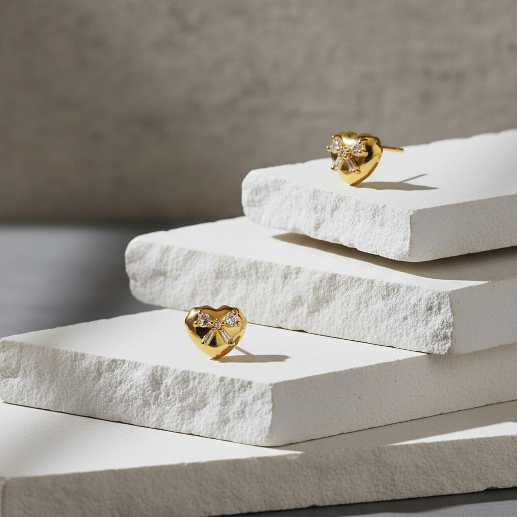 Gold heart-shaped earrings on white stone blocks with a neutral background
