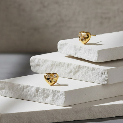 Gold heart-shaped earrings on white stone blocks with a neutral background