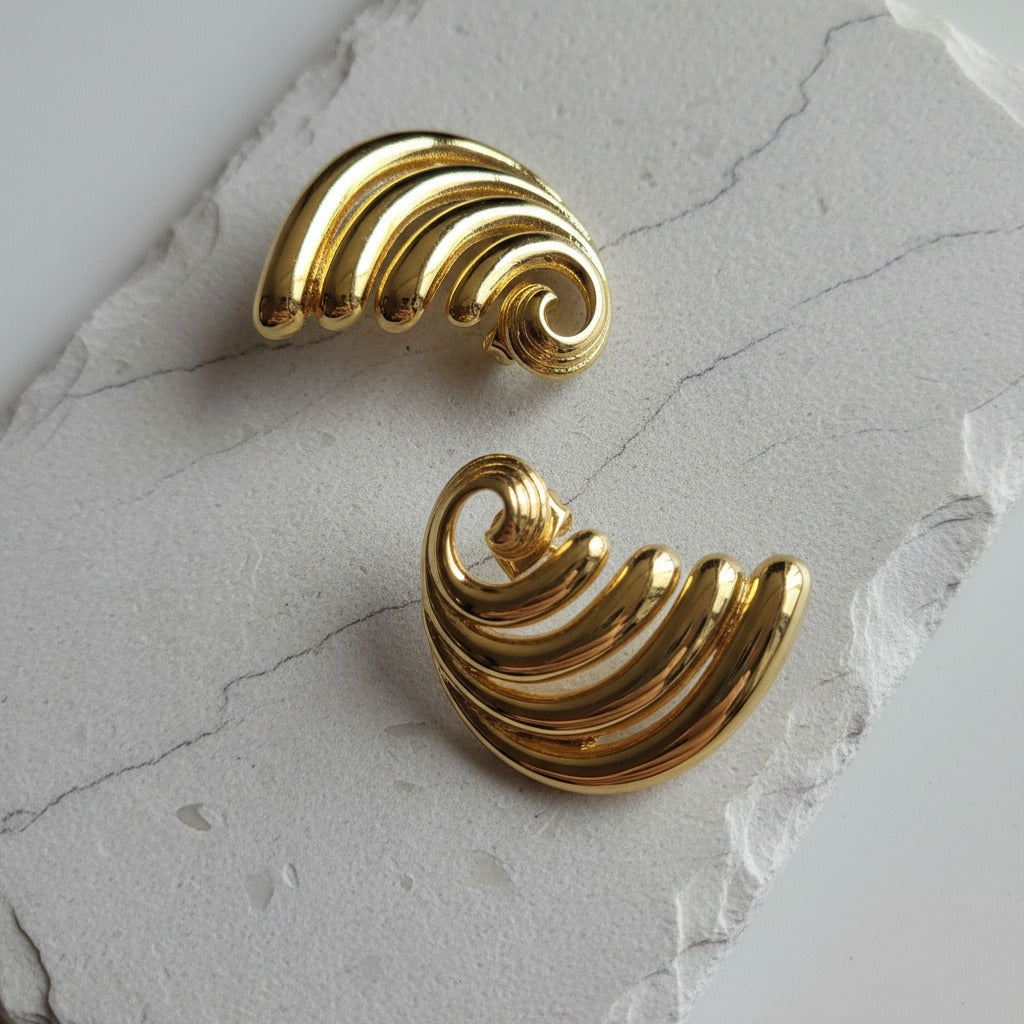 Pair of gold spiral earrings on a light gray stone surface