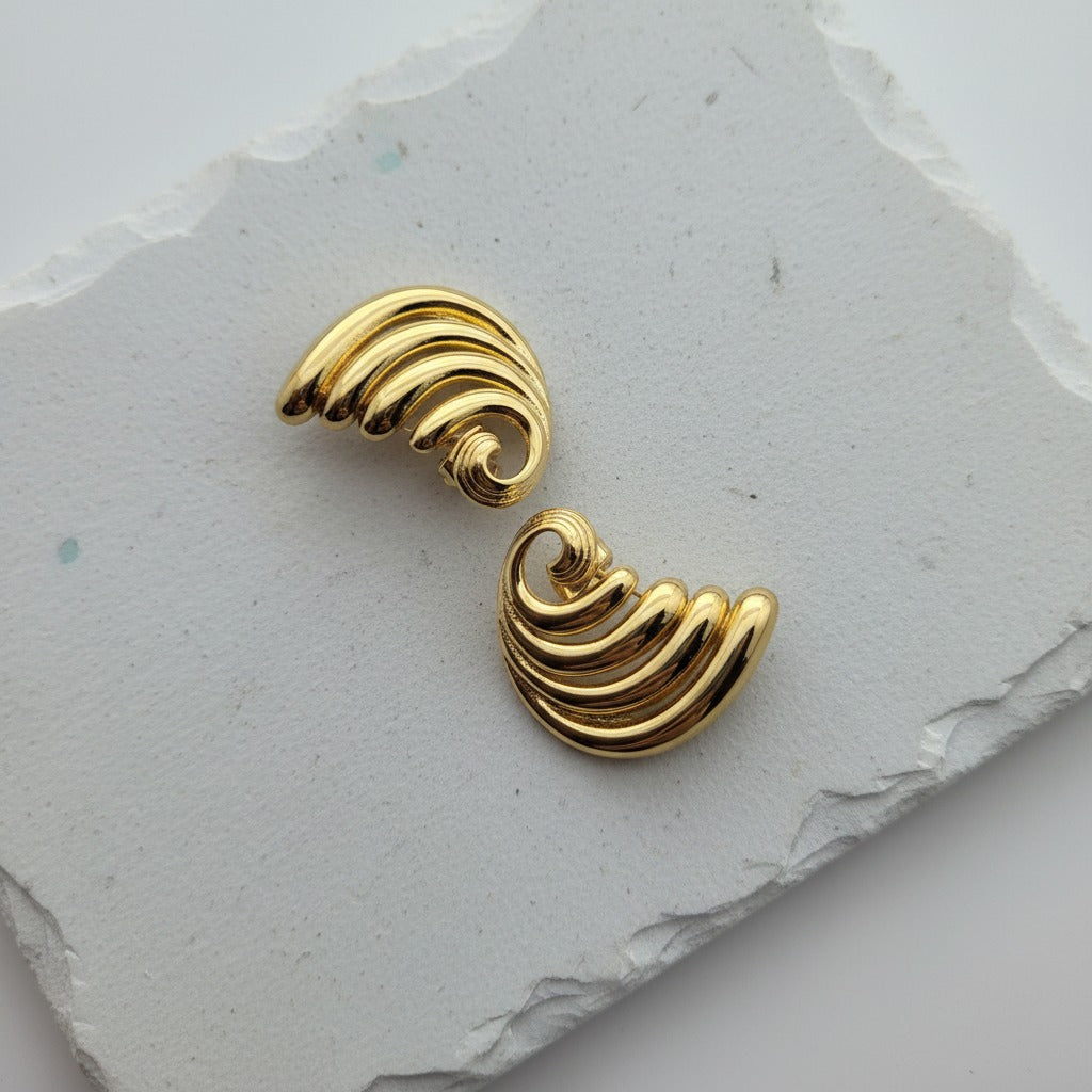 Gold wave-shaped earrings on a textured gray surface