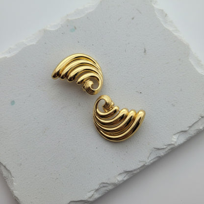 Gold wave-shaped earrings on a textured gray surface