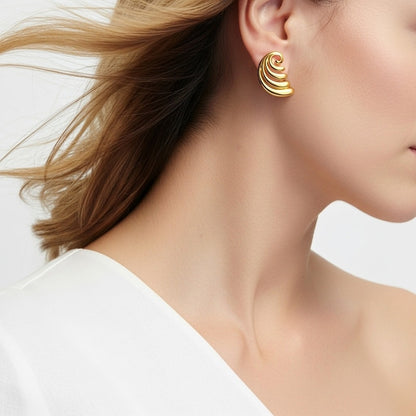 Close-up of a person wearing gold spiral earrings on a plain background