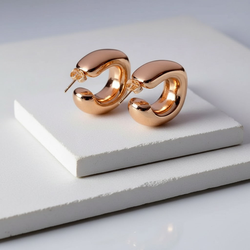Rose gold hoop earrings on a white platform