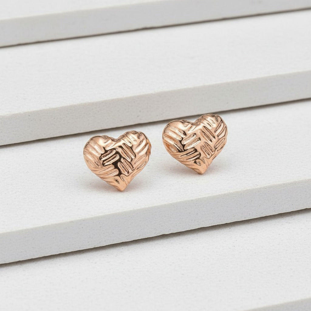Rose gold heart-shaped earrings on a light wooden surface