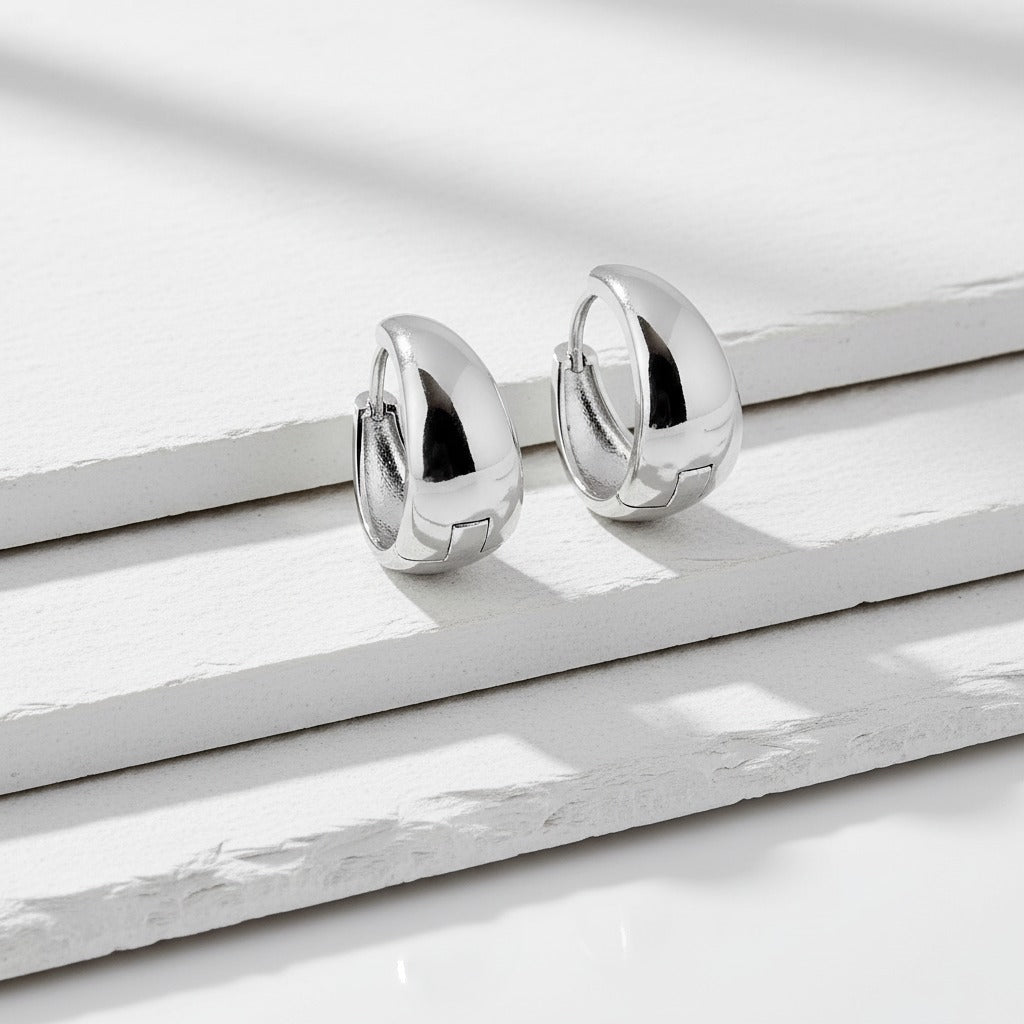 Pair of silver hoop earrings on a white marble surface