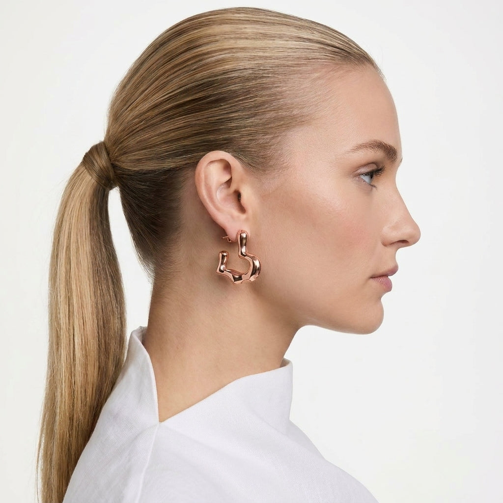 Woman with a ponytail wearing rose gold hoop earrings on a light Rose gold hoop earrings on a light gray background premium stainless steel hypoallergenic, waterproof, tarnish-proof, and light weight 