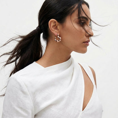 Woman wearing a white top with cut-out design on a plain background Rose gold hoop earrings on a light gray background premium stainless steel hypoallergenic, waterproof, tarnish-proof, and lightweight