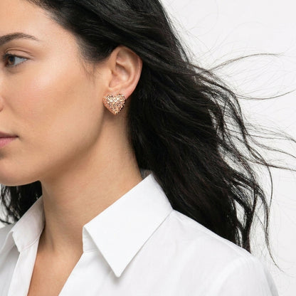 Close-up of a woman wearing rose gold heart-shaped earrings with a white shirt Medium Rose Gold Amora Heart Stud Earrings premium stainless steel hypoallergenic, waterproof, tarnish-proof, and lightweight.