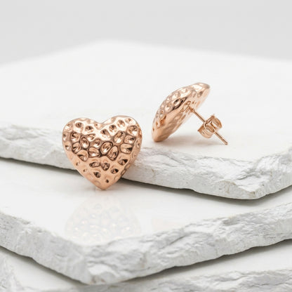 Rose gold heart-shaped earrings on a light stone surface Medium Rose Gold Amora Heart Stud Earrings premium stainless steel hypoallergenic, waterproof, tarnish-proof, and lightweight