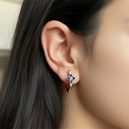 Gold earring with a blue gemstone worn by a person with dark hair.