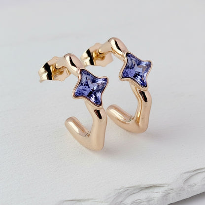 Gold earrings with star-shaped purple gemstones on a light gray background