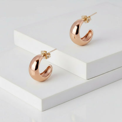 Rose gold hoop earrings on a white geometric platform