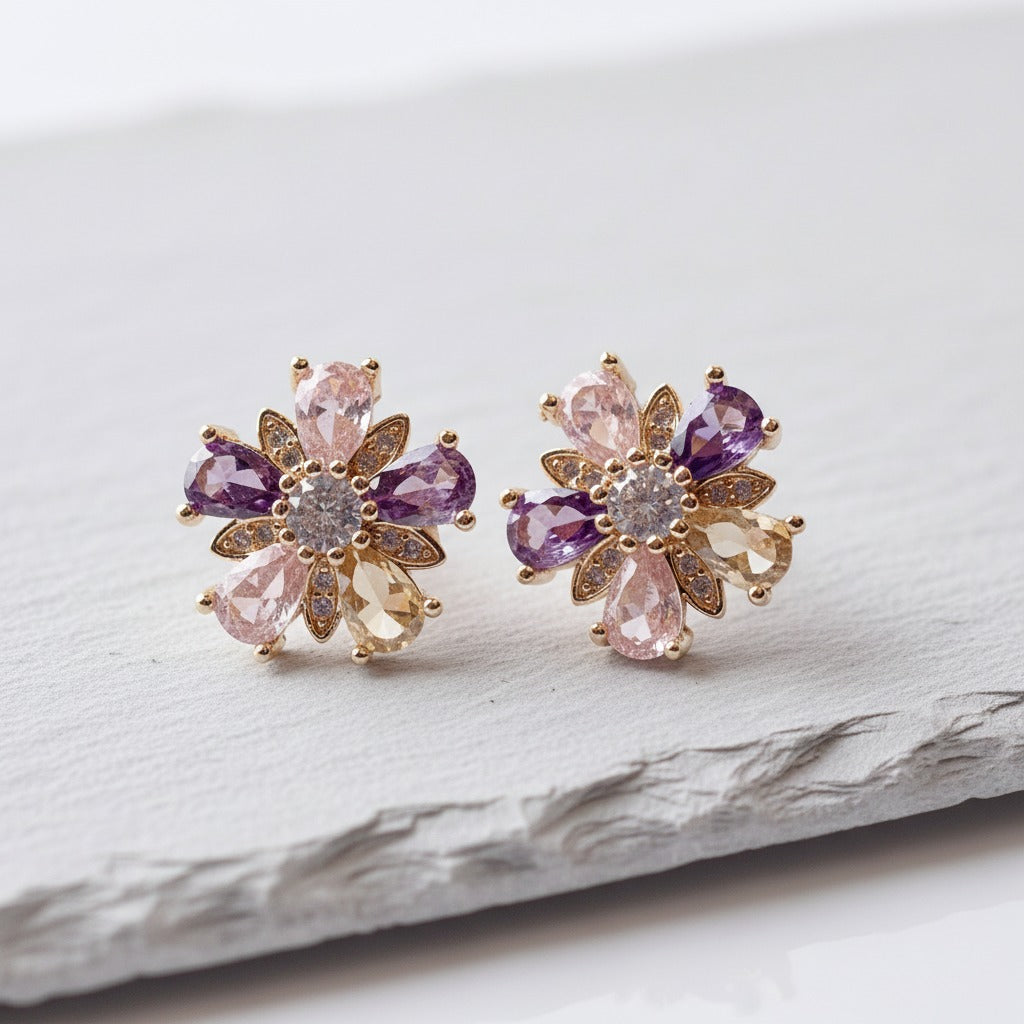 Pair of floral earrings with purple and pink gemstones on a light background