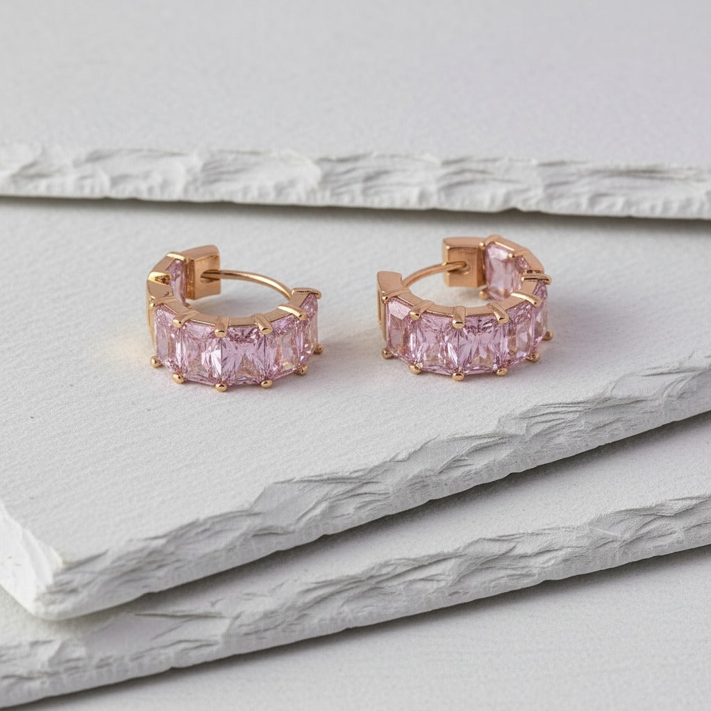 Rose gold hoop earrings with pink gemstones on a marble surface