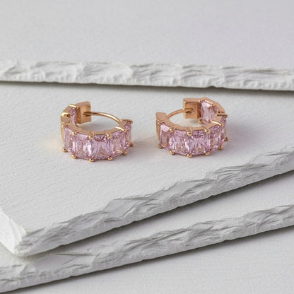 Rose gold hoop earrings with pink gemstones on a marble surface