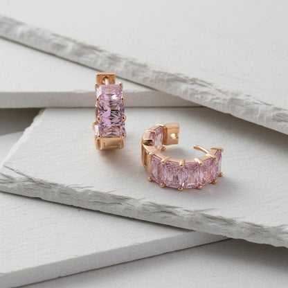 Rose gold hoop earrings with pink gemstones on a light gray surface