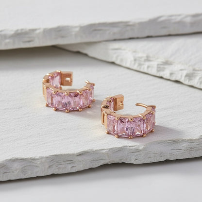 Rose gold hoop earrings with pink gemstones on a light stone surface