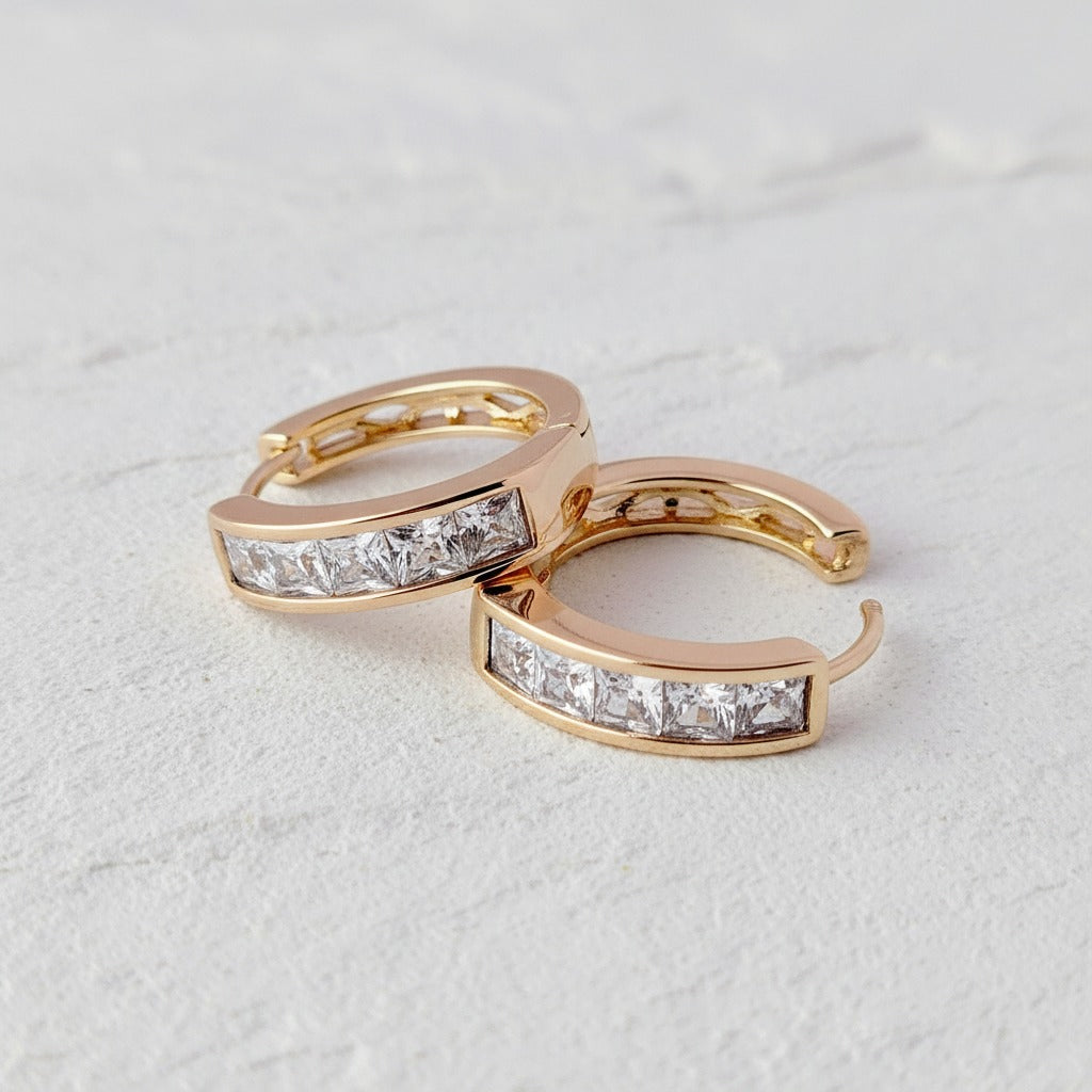 Pair of gold hoop earrings with diamond accents on a light gray background