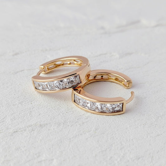 Pair of gold hoop earrings with diamond accents on a light gray background