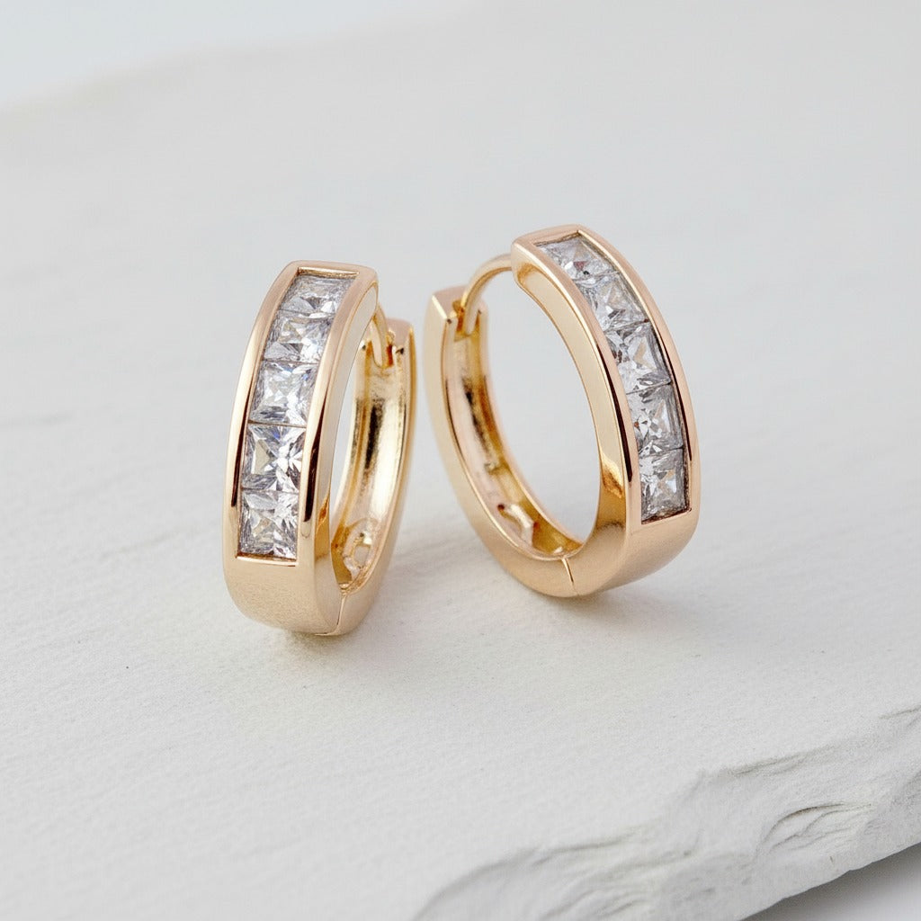 Gold hoop earrings with clear gemstones on a light gray background
