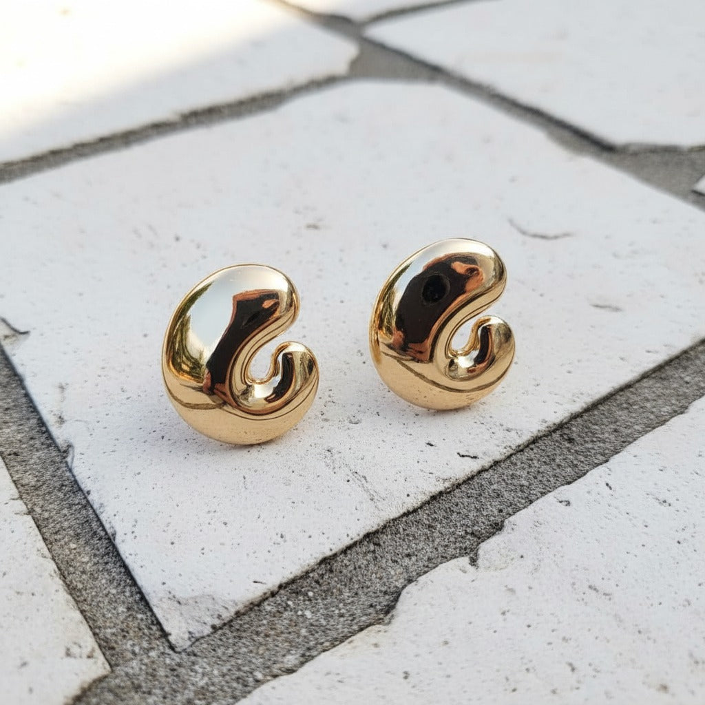 Gold spiral earrings on a stone surface