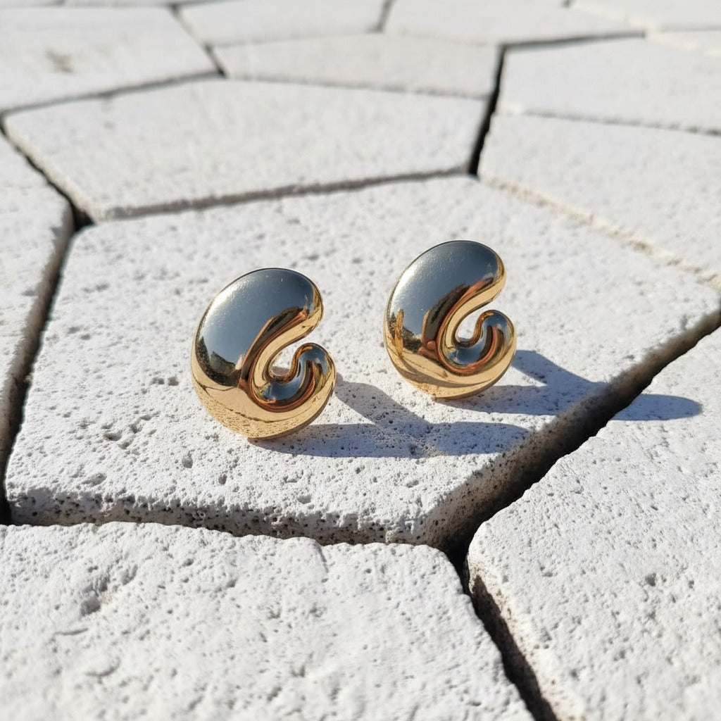 Gold spiral earrings on a textured stone surface