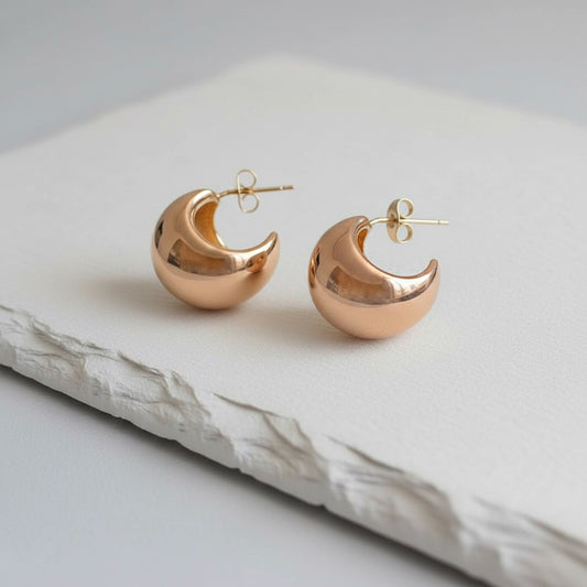 Rose gold crescent moon earrings on a light gray surface