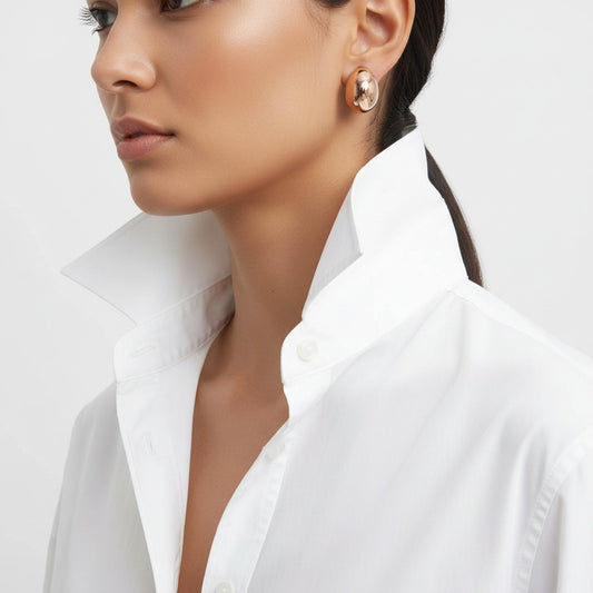 Close-up of a woman wearing gold earrings with a white shirt background