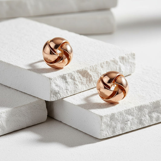 Rose gold knot earrings on a light stone surface