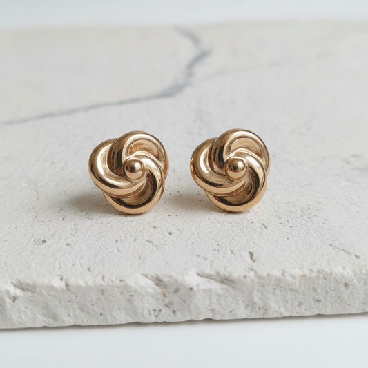 Pair of gold knot earrings on a light stone surface