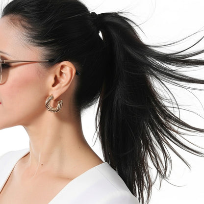 Woman with black hair in a ponytail wearing gold hoop earrings on a white background