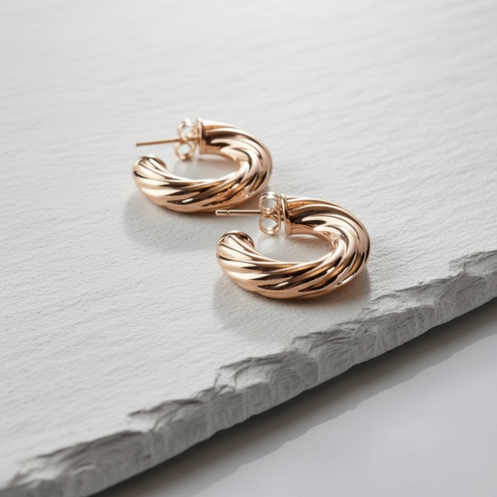 Rose gold hoop earrings on a light gray stone surface