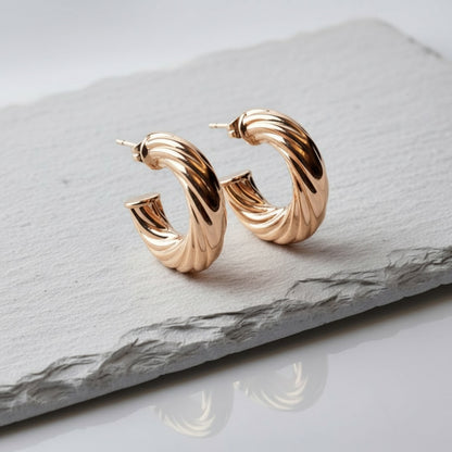 Rose gold hoop earrings on a gray stone surface