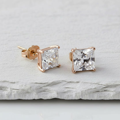 Rose gold square-cut stud earrings on a light gray stone surface