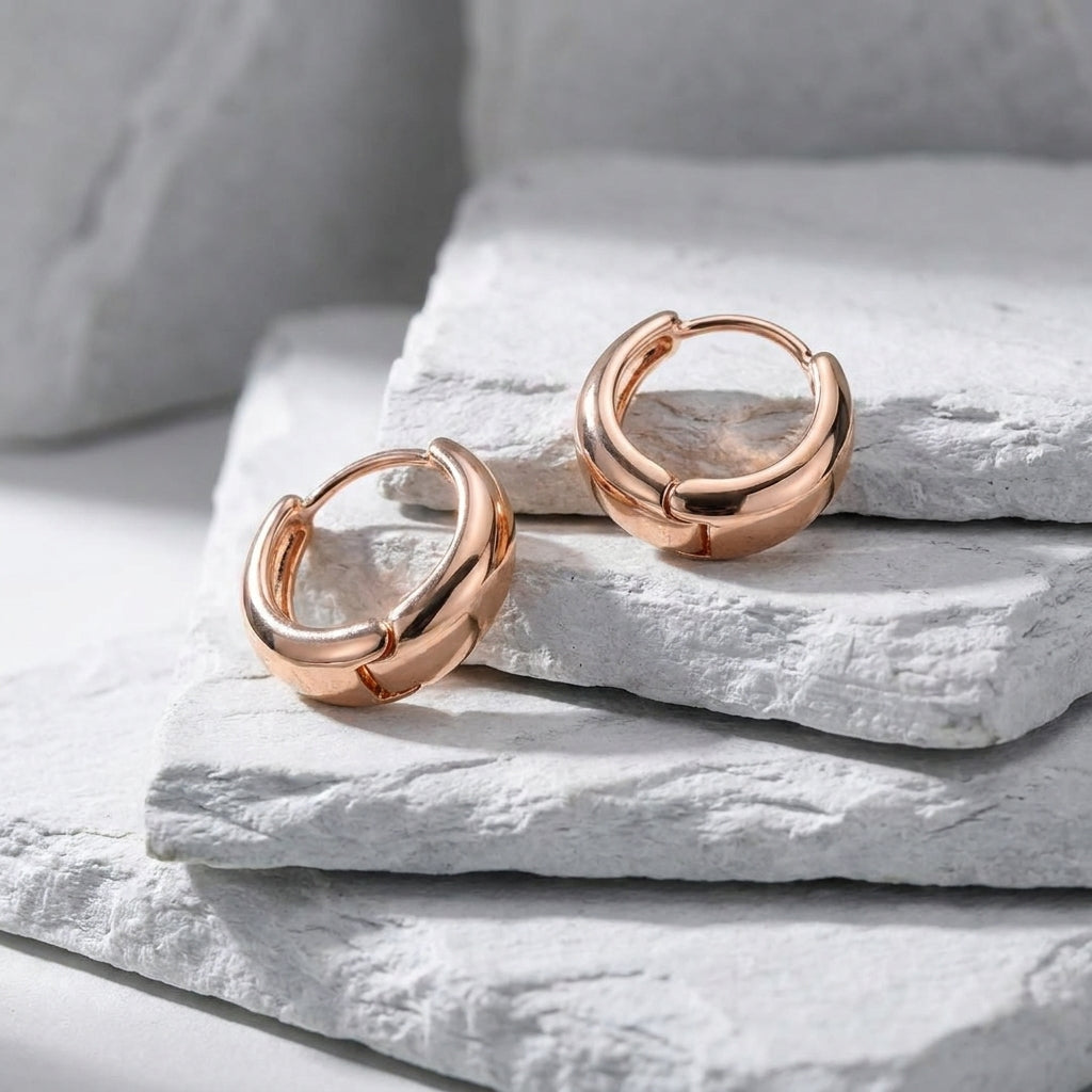 Rose gold hoop earrings on a textured white surface Small Rose Gold Pure Huggie Earrings premium stainless steel waterproof, tarnish-proof, hypoallergenic, and lightweight—perfect for sensitive ears and everyday wear.