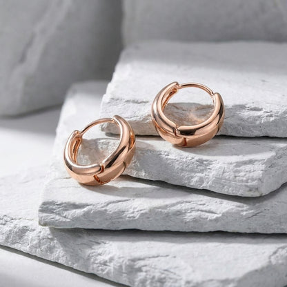 Rose gold hoop earrings on a textured white surface Small Rose Gold Pure Huggie Earrings premium stainless steel waterproof, tarnish-proof, hypoallergenic, and lightweight—perfect for sensitive ears and everyday wear.