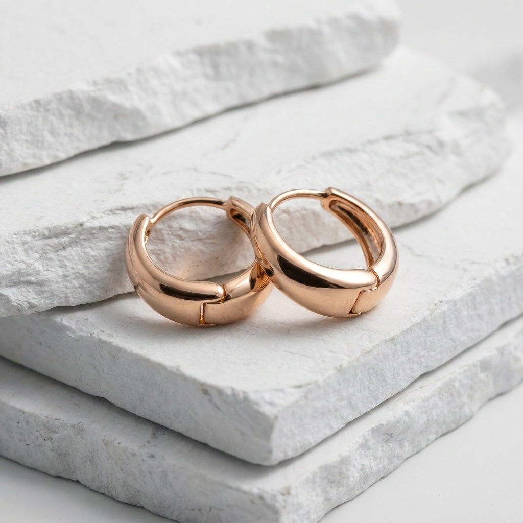 Rose gold hoop earrings on a light stone surface Small Rose Gold Pure Huggie Earrings premium stainless steel waterproof, tarnish-proof, hypoallergenic, and lightweight—perfect for sensitive ears and everyday wear.