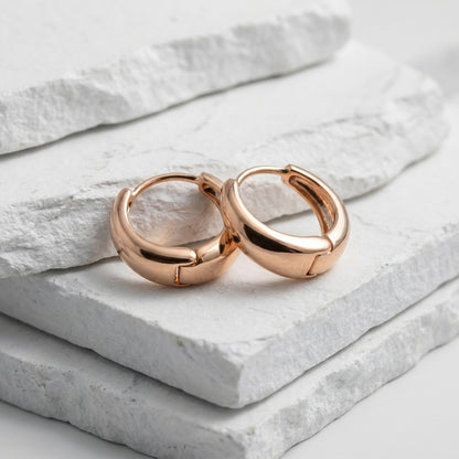 Rose gold hoop earrings on a light stone surface Small Rose Gold Pure Huggie Earrings premium stainless steel waterproof, tarnish-proof, hypoallergenic, and lightweight—perfect for sensitive ears and everyday wear.