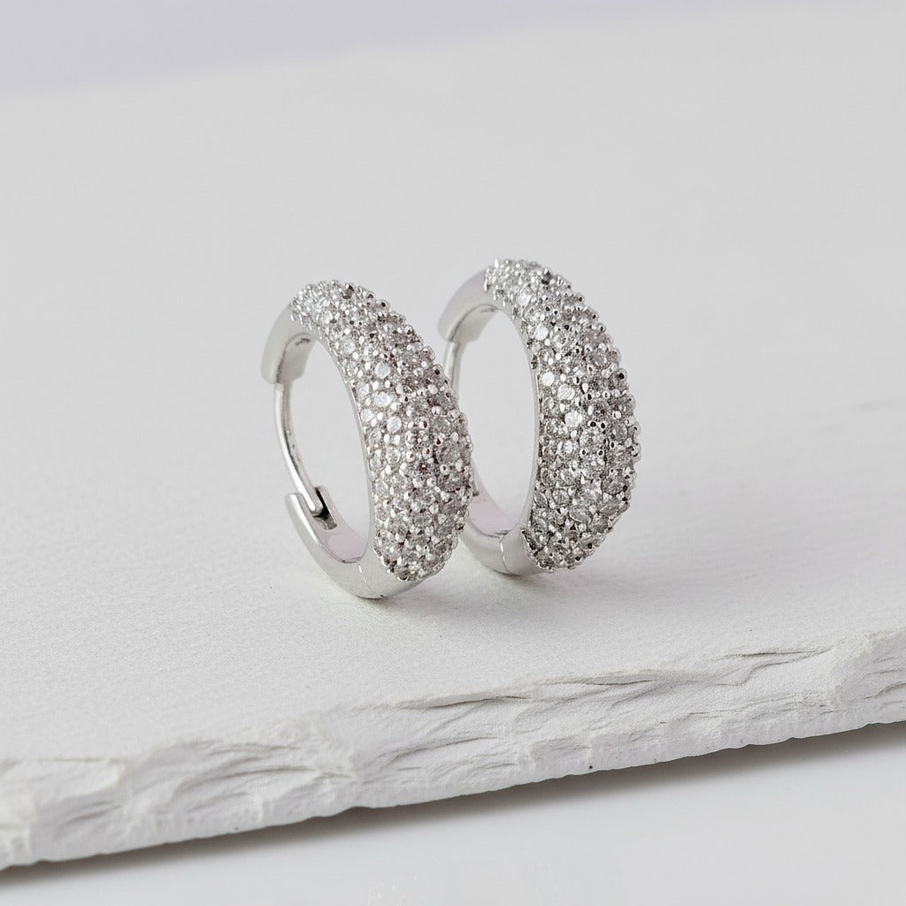 Pair of silver hoop earrings with embedded stones on a light gray surface.