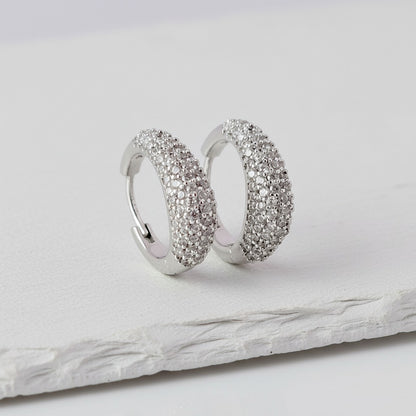 Pair of silver hoop earrings with embedded stones on a light gray surface.